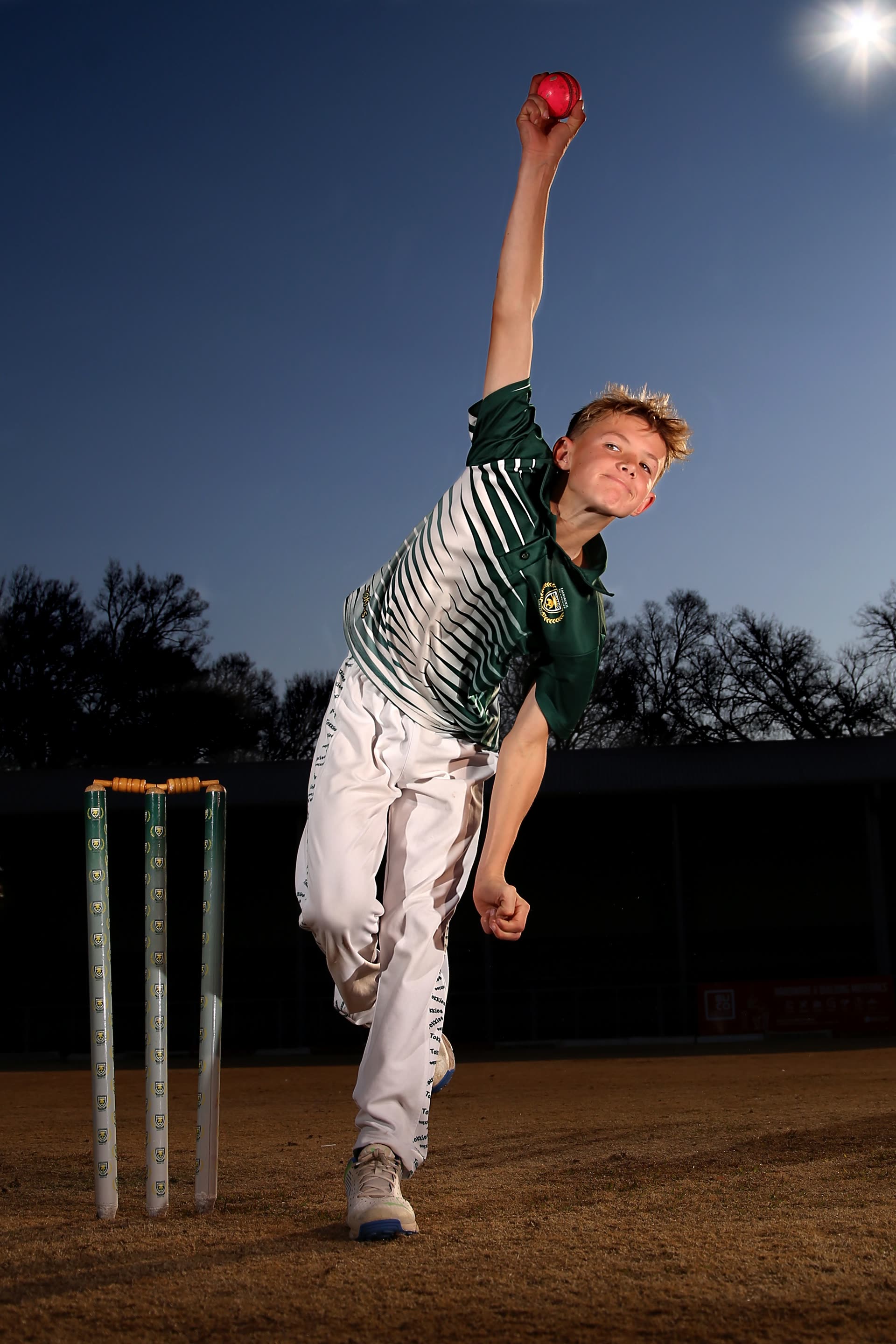 Bowler frozen at the moment of delivery against a dusk sky
