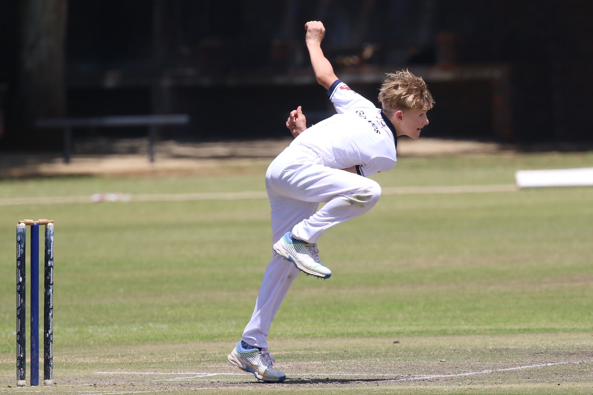 Fast bowler mid-delivery stride on a cricket pitch, filmed side-on