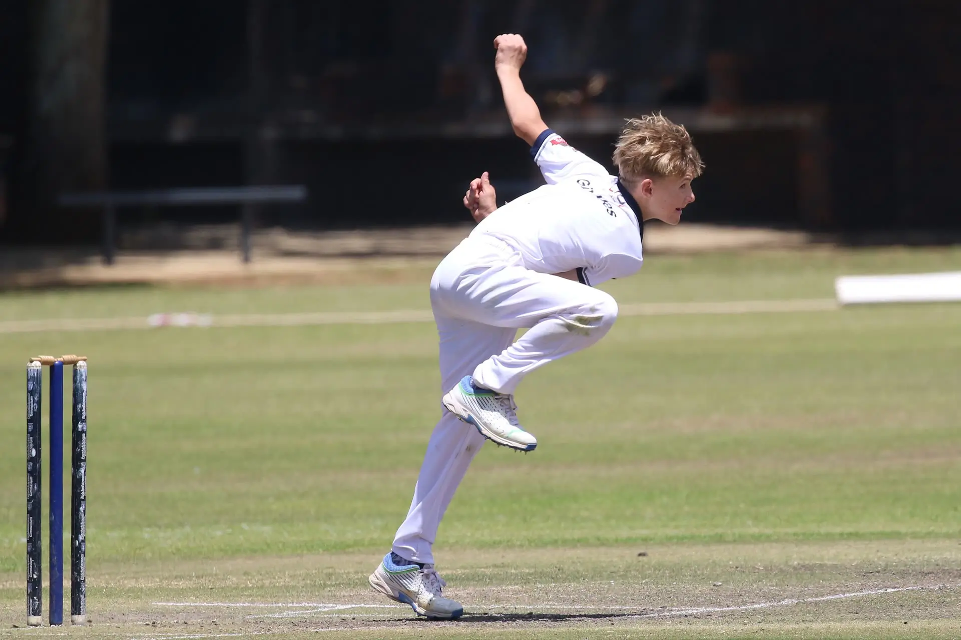 Fast bowler mid-delivery stride on a cricket pitch, filmed side-on